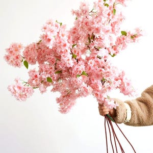 May include: A bouquet of pink artificial cherry blossom branches with green leaves. The branches are held together with brown wire stems.