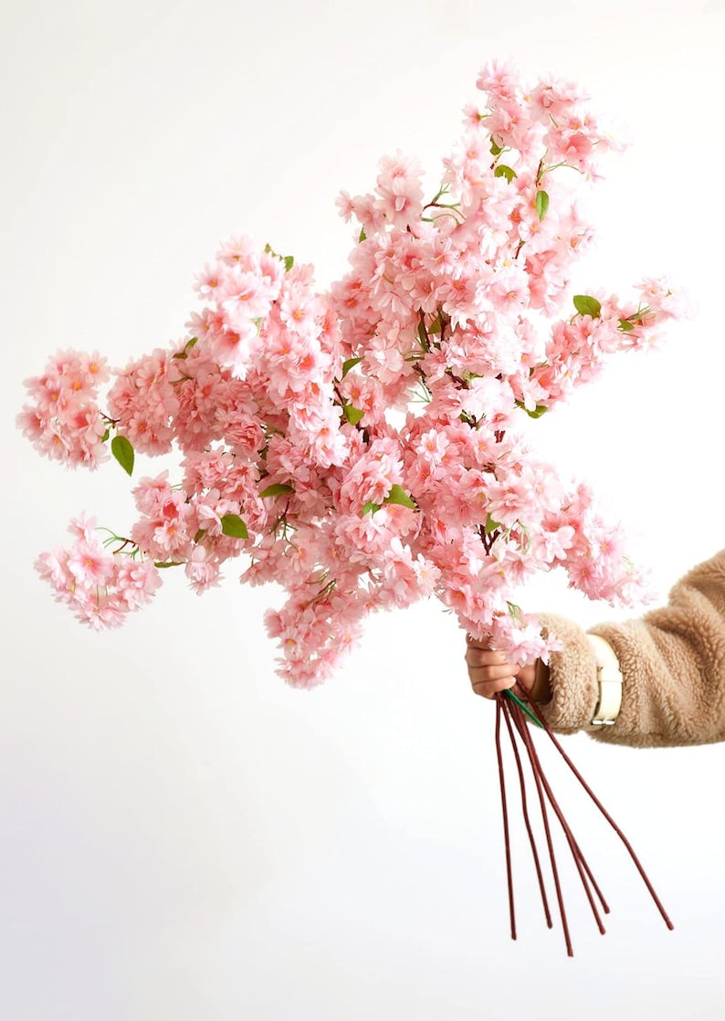 May include: A bouquet of pink artificial cherry blossom branches with green leaves. The branches are held together with brown wire stems.