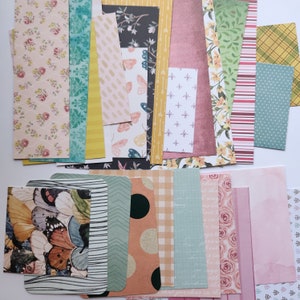 Pode incluir: Uma cole&ccedil;&atilde;o de folhas de papel retangulares com diversos padr&otilde;es, incluindo estampas florais, borboletas, formas geom&eacute;tricas, listras, bolinhas e cores s&oacute;lidas em tons de rosa, verde, amarelo, azul e marrom para projetos de artesanato.