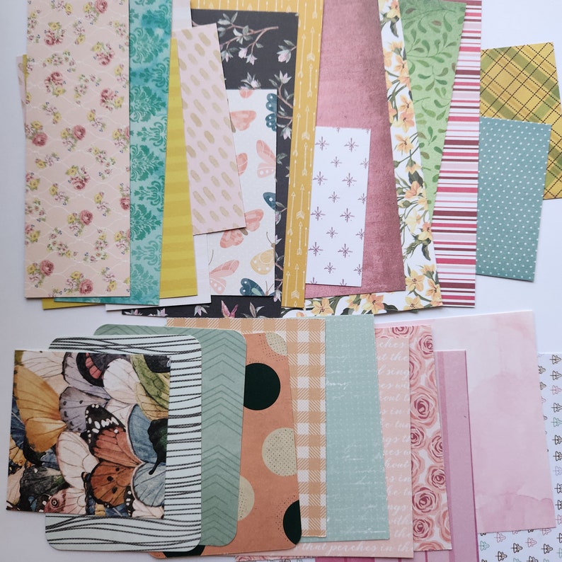 Pode incluir: Uma cole&ccedil;&atilde;o de folhas de papel retangulares com diversos padr&otilde;es, incluindo estampas florais, borboletas, formas geom&eacute;tricas, listras, bolinhas e cores s&oacute;lidas em tons de rosa, verde, amarelo, azul e marrom para projetos de artesanato.