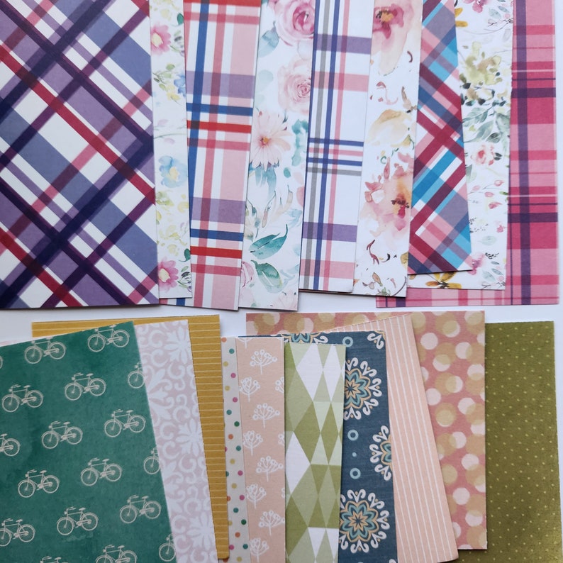 Pode incluir: Uma cole&ccedil;&atilde;o de folhas de papel retangulares com padr&otilde;es diversos, incluindo xadrez roxo e vermelho, estampas florais em aquarela, motivos de bicicletas verdes, listras amarelas, formas geom&eacute;tricas, mandalas azuis e bolinhas coloridas.