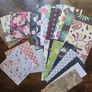 Pode incluir: Uma cole&ccedil;&atilde;o de folhas de papel retangulares com padr&otilde;es diversos, incluindo rosas cor-de-rosa, folhas verdes, bolinhas, paisley e ilustra&ccedil;&otilde;es bot&acirc;nicas. O sortido inclui v&aacute;rias paletas de cores como castanho escuro, creme, rosa claro e verde azeitona.