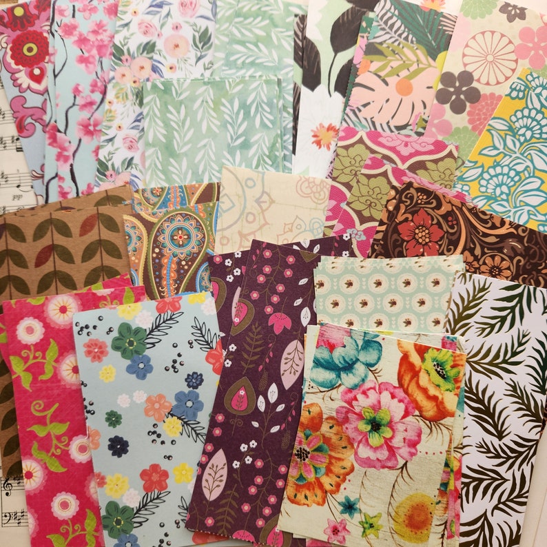 Pode incluir: Uma cole&ccedil;&atilde;o de folhas de papel retangulares com uma gama diversificada de padr&otilde;es, incluindo designs florais, paisley, bot&acirc;nicos e geom&eacute;tricos em cores vibrantes como rosa, azul, verde, amarelo, castanho e branco, dispostos em pilha.