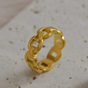 A gold ring with a unique chain-like design is placed on a white surface.