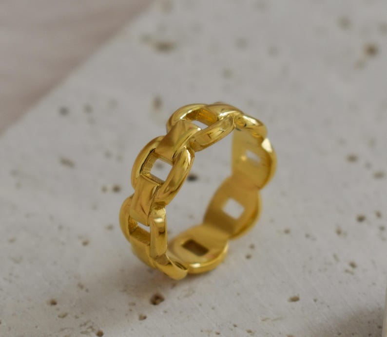 A gold ring with a unique chain-like design is placed on a white surface.