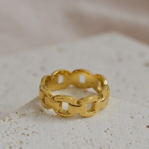 A gold chain ring is placed on a white surface.