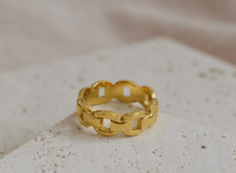 A gold chain ring is placed on a white surface.