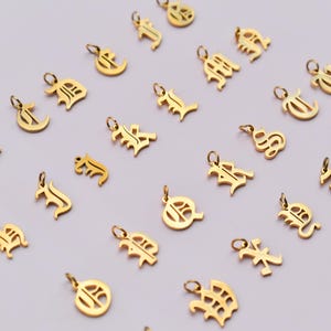 a collection of gold-colored charms or pendants, each featuring a different letter or symbol, arranged in a grid-like pattern on a light background.