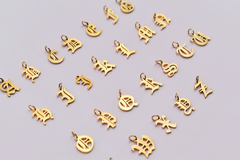 a collection of gold-colored charms or pendants, each featuring a different letter or symbol, arranged in a grid-like pattern on a light background.