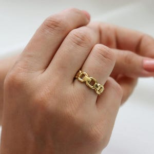 A close-up of a person's hand wearing a gold ring on the ring finger.