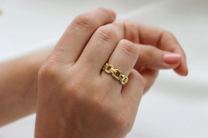 A close-up of a person's hand wearing a gold ring on the ring finger.