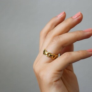 A close-up of a person's hand wearing a gold ring, with their fingers slightly curled and the ring visible.