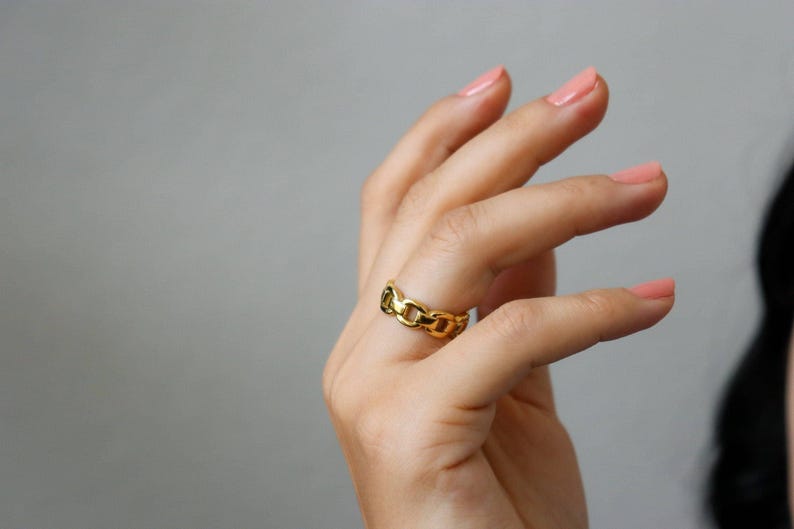 A close-up of a person's hand wearing a gold ring, with their fingers slightly curled and the ring visible.