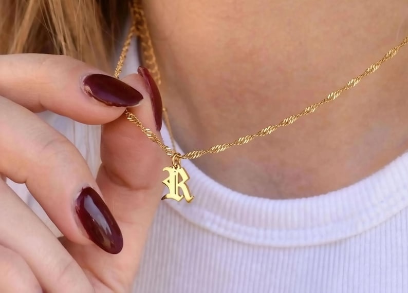 A close-up of a person's hand wearing a gold necklace with a small pendant.