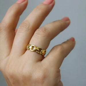 A close-up of a person's hand wearing a gold ring with a chain-link design.