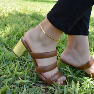 A close-up view of a person's feet wearing brown strappy sandals on a grassy lawn.