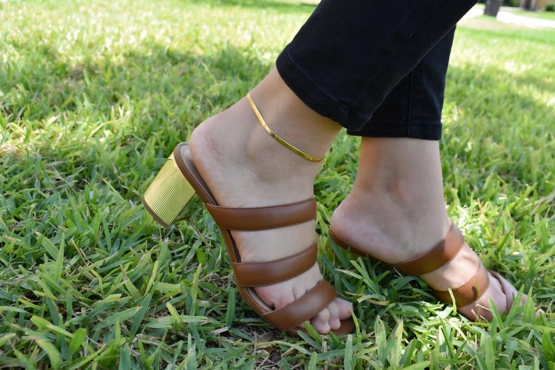 A close-up view of a person's feet wearing brown strappy sandals on a grassy lawn.