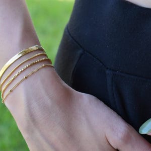 A close-up view of a person's wrist wearing multiple gold bracelets.