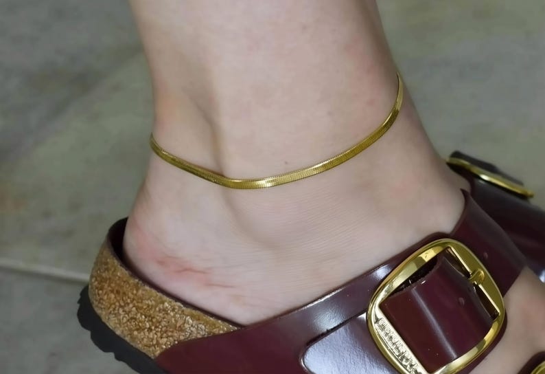 A close-up of a person's foot wearing a pair of burgundy sandals with gold buckles.