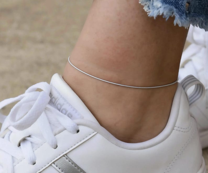 A close-up view of a person's ankle wearing a silver ankle bracelet.