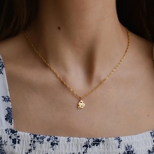 A close-up view of a woman's neck and chest area, showing a gold necklace with a small pendant.