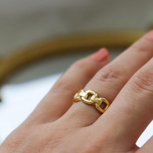 A close-up view of a person's hand wearing a gold ring with a chain-link design.
