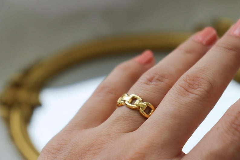 A close-up view of a person's hand wearing a gold ring with a chain-link design.