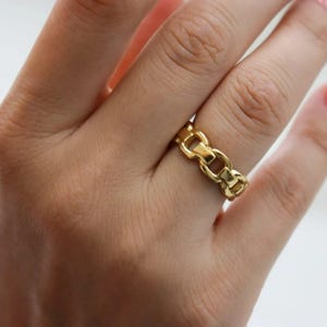 A close-up of a person's hand wearing a gold ring with a chain-link design.
