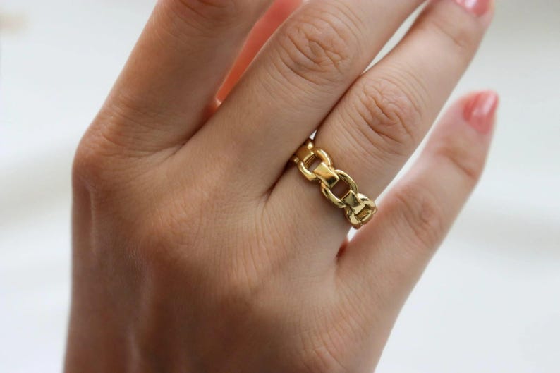 A close-up of a person's hand wearing a gold ring with a chain-link design.