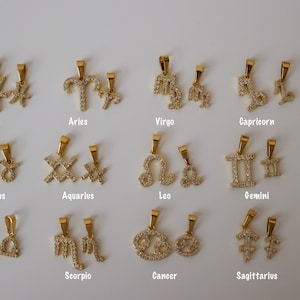 May include: Twelve gold zodiac sign pendants with clear rhinestone accents. Each pendant features a different zodiac symbol, including Pisces, Aries, Virgo, Capricorn, Taurus, Aquarius, Leo, Gemini, Libra, Scorpio, Cancer, and Sagittarius.