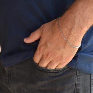 A close-up view of a person's hand in a pocket, wearing a blue shirt and silver bracelet.