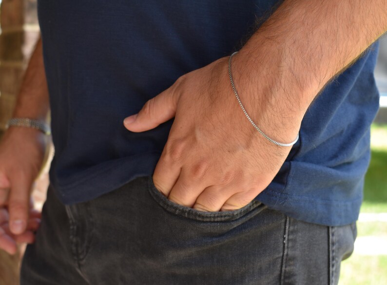 A close-up view of a person's hand in a pocket, wearing a blue shirt and silver bracelet.