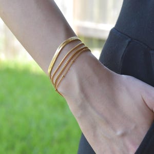 A close-up view of a person's wrist wearing multiple gold-colored bracelets.