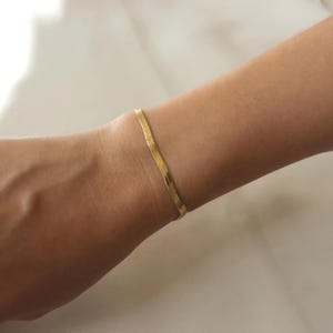 A gold bracelet is worn on a person's wrist.