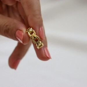 A close-up of a person's hand holding a small gold chain with a clasp, against a white background.