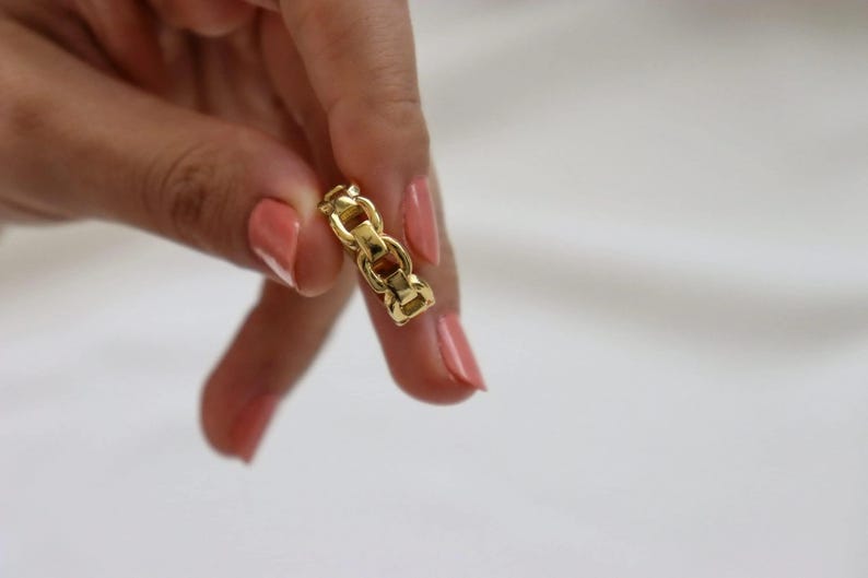 A close-up of a person's hand holding a small gold chain with a clasp, against a white background.
