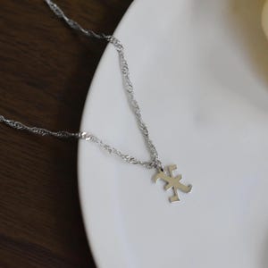 Two silver necklaces with pendants are displayed on a white plate, with a white candle in the background.