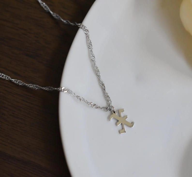Two silver necklaces with pendants are displayed on a white plate, with a white candle in the background.