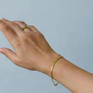 A close-up view of a person's hand wearing a gold bracelet and a ring on their finger.