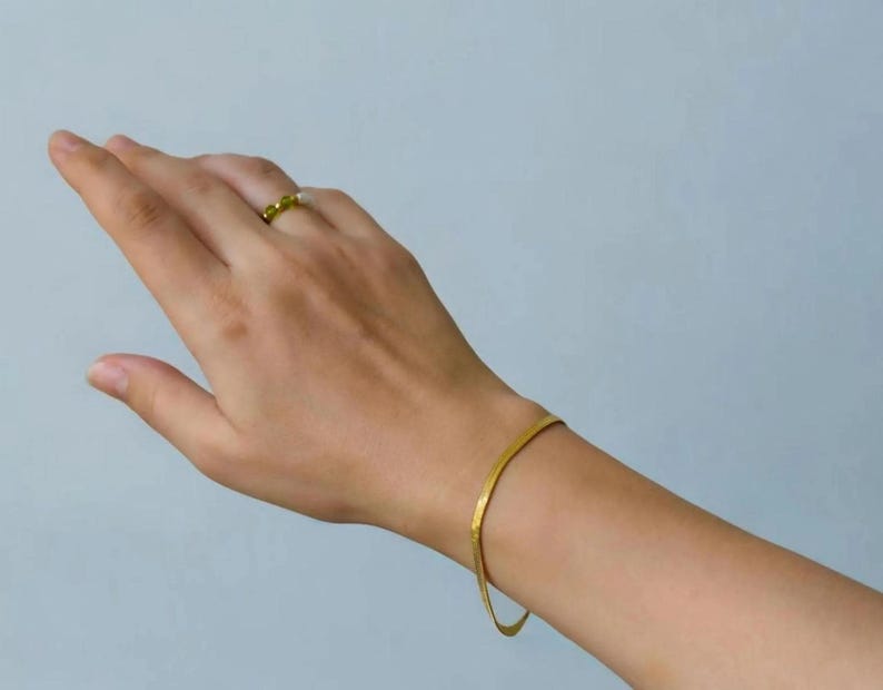 A close-up view of a person's hand wearing a gold bracelet and a ring on their finger.