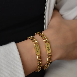 May include: Two gold chain bracelets with engraved rectangular tags. The tag on the top bracelet reads "444" and the tag on the bottom bracelet reads "222".