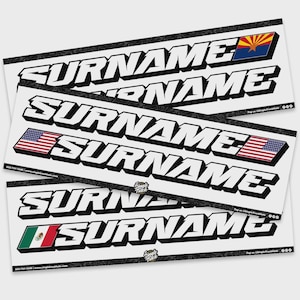 May include: White vinyl decals with the word "SURNAME" in bold, black, 3D lettering. Some decals feature the Arizona flag, the American flag, and the Mexican flag. The decals are arranged on a white background.