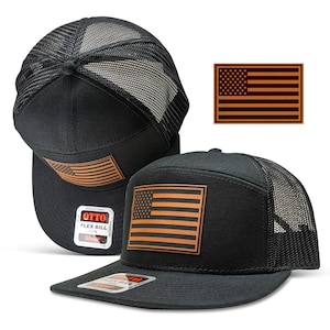 May include: Black trucker hat with a brown leather American flag patch. The hat has a mesh back and a flex bill. The patch is sewn on the front of the hat.
