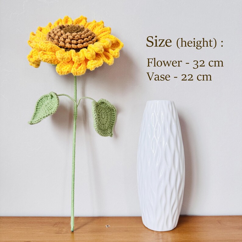 May include: A crocheted sunflower with green leaves in a white ceramic vase. The sunflower is 32 inches tall and the vase is 22 inches tall. Size (height): Flower - 32 cm Vase - 22 cm