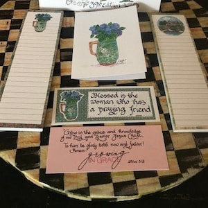 May include: Three white notepads with lined paper and a floral design. The notepads have the text "Blessed is the woman who has a praying friend" and "Grow in the grace and knowledge of our Lord, and Savior Jesus Christ. To him be glory both now and forever! Amen. Growing in Grace 2 Peter 3:18".
