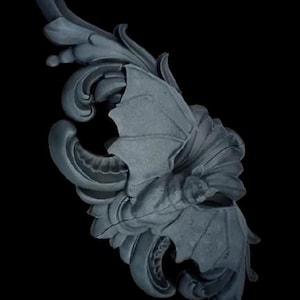 May include: A detailed, gray-blue decorative element with a bat-wing design. The ornate piece features swirling leaves and a central bat figure, set against a black background. The sculpture has a textured surface.