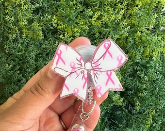 May include: A pink ribbon patterned badge reel with a pink glitter charm. The reel is attached to a clear plastic retractable cord.