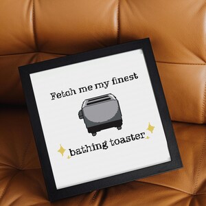 May include: Black framed art print with the text "Fetch me my finest bathing toaster" and a pixelated toaster graphic. The print is on a white background and has yellow star accents.