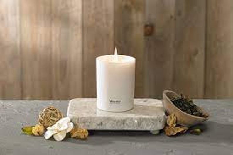 May include: White candle on a white marble tray with dried flowers and a small bowl of green tea leaves.