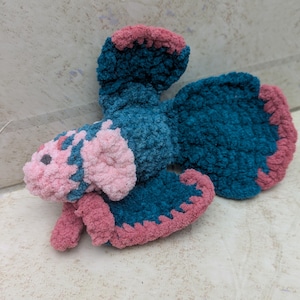 Peut inclure: Une peluche faite à la main en forme de papillon. Le papillon est fait de fil doux et texturé de couleur bleu sarcelle et rose. Les ailes et la tête sont bleu sarcelle, avec des accents roses sur les bords et le visage.
